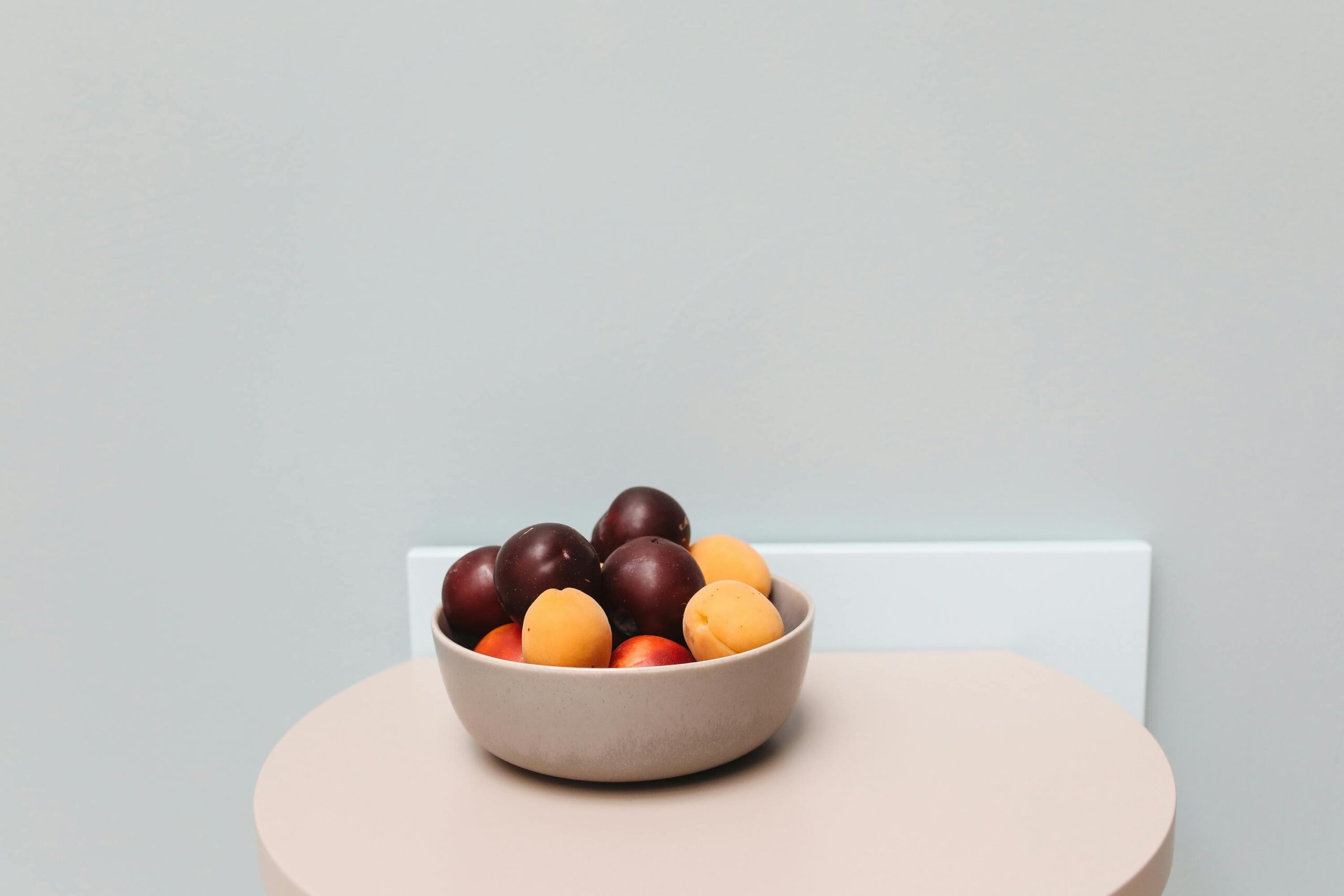 A beige bowl filled with fresh plums and apricots on a minimalist table, perfect for food-themed projects.